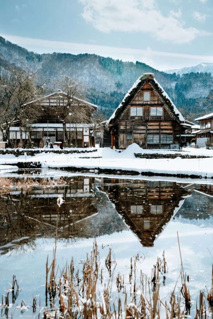 Snow-covered gassho-zukuri farmhouse in Shirakawa-go reflected in a pond under a blue winter sky